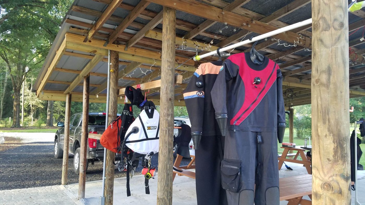 Drysuits and a wing hanging to dry under the pavilion