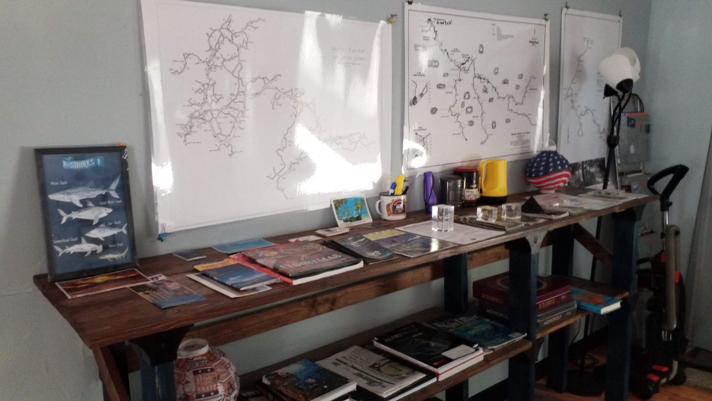 Cave maps on the wall over a table of dive books and magazines